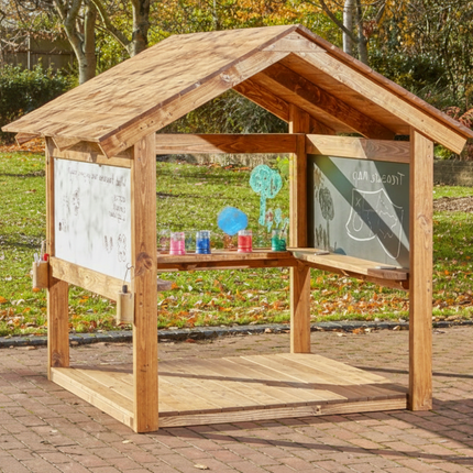 Wooden outdoor playhouse with whiteboard, chalkboard, and colorful cups on a brick patio.