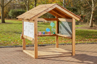 Wooden outdoor playhouse with whiteboard, chalkboard, and colorful cups on a brick patio.