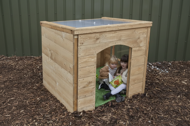 Two children playing inside a wooden playhouse on mulch.