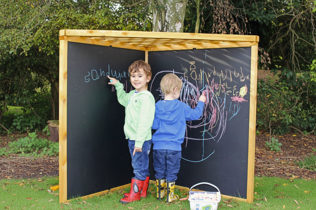 Two children drawing on an outdoor chalkboard with a wooden frame.