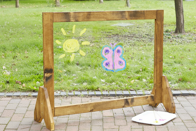Wooden frame with child's drawings of a sun and butterfly on a grassy background