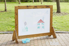 Wooden outdoor whiteboard with children's drawings on a grassy background