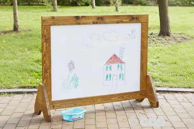 Wooden outdoor whiteboard with children's drawings on a grassy background