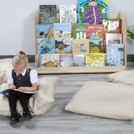 Child sitting on a bean bag reading a book in front of a bookshelf with children's books.