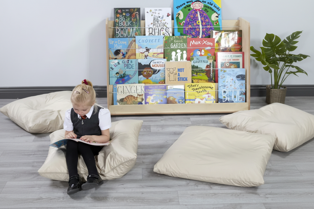 Child sitting on a bean bag reading a book in front of a bookshelf with children's books.