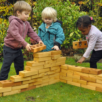 Children playing with wooden building blocks outdoors in a garden setting.