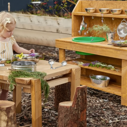 Child playing with a wooden play kitchen set outdoors.