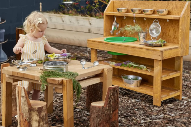 Child playing with a wooden play kitchen set outdoors.