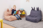 Child reading a book on a pink bean bag chair with a gray rug and blue bean bag chair in the background.