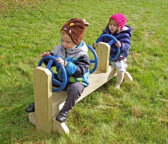 Two children playing on a seesaw in a grassy area
