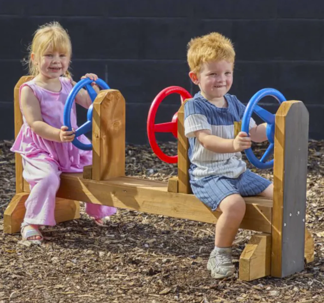 Two children playing on a wooden playground structure with colorful handles.